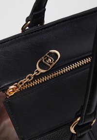 Borsa a mano in pelle nera con una zip dorata e un tirante a catena, texture liscia e dettagli in metallo. Design compatto con forma strutturata.