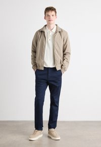 Beige bomber jacket with ribbed cuffs, cream polo shirt, navy pants, and tan sneakers with white soles. Simple, modern design and neutral colors.