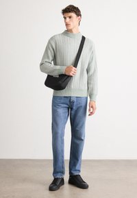 Light green knitted sweater with textured pattern, blue jeans, and black shoes. Black shoulder bag with logo. Simple, casual outfit.