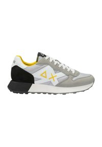 Zapatilla deportiva gris con acentos en blanco y negro, que presenta una parte superior texturizada, una suela acolchada y un detalle amarillo en el cuello.