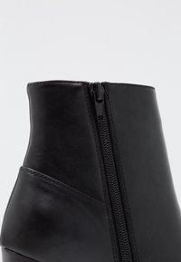 Stivale alla caviglia in pelle nera con cerniera laterale, texture liscia e design elegante e moderno. Nessun motivo visibile o dettagli in metallo.