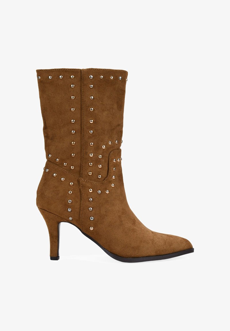 Botín de ante marrón hasta el tobillo con punta afilada y tacón delgado, con tachuelas metálicas a los lados y en la parte frontal para un detalle adicional.