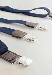 Tengerész stílusú felfüggesztők texturált anyagból, barna bőr részletekkel és ezüstszínű fém kapcsokkal. Három állítható szakasz sorban elhelyezve.