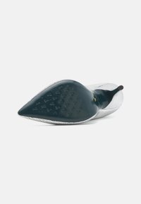 Zapato de tacón con punta afilada en cuero plateado agrietado. Suela oscura lisa con patrón decorativo. Con un tacón delgado y un diseño minimalista.