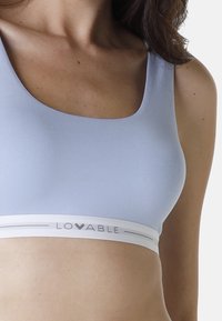 Bra sportivo azzurro chiaro realizzato in tessuto morbido, con una ampia fascia bianca riportante il logo "LOVABLE". Scollatura a U e senza padding visibile.