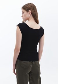 Svart ribbad kortärmad topp med rundad halsringning, åtsittande design och slät textur, bärs med olivgröna byxor, visar bakvy.