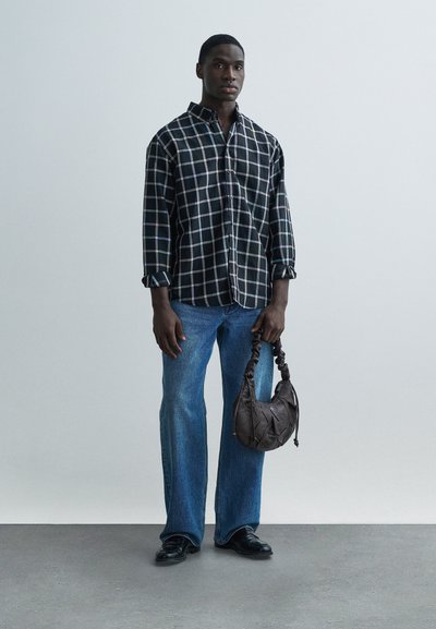 Μαύρο-άσπρο καρό πουκάμισο, άνετο μπλε τζιν, κρατώντας καφέ τσάντα με υφή, μαύρα παπούτσια, πάνω σε ουδέτερο φόντο.