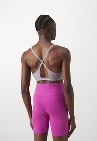 Grå sportbh med korsad ryggdesign och underbandsetikett, kombinerad med högmidjade rosa shorts, slät tyg, figurnära passform.