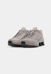 Heledad hallhalli jooksujalatsid, millel on tekstuuriga pealmine osa, nööridega kinnitussüsteem ja must segmenteeritud tald; sisaldab swoosh logo ja väikeseid aktsente.