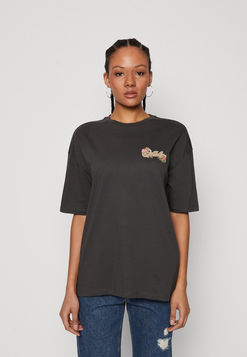 Μαύρο βαμβακερό μπλουζάκι με υπερμεγέθη εφαρμογή, στρογγυλή λαιμόκοψη και λουλουδάτο γραφικό στην αριστερή πλευρά. Συνδυασμένο με ανοιχτό μπλε σκισμένα τζιν.