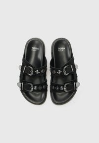 Black slide sandals with two wide straps, buckle accents, and decorative studs. Made of leather and suede with a smooth finish.