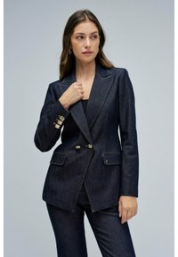 Blazer de denim oscuro con un corte ajustado, solapas con muesca, botones dobles dorados y bolsillos laterales. Tejido texturizado y forma estructurada.