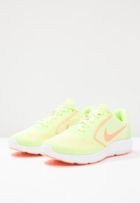 Baskets de sport jaune néon avec un dessus en mesh, accents orange et semelle en caoutchouc blanc. Présente des lacets et le logo Nike sur le côté.