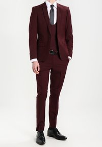 Bordowy garnitur trzyczęściowy o slim fit, jednorzędowa marynarka z klapami w kształcie notch oraz dopasowane spodnie. Czarne buty wizytowe dopełniają zestaw.