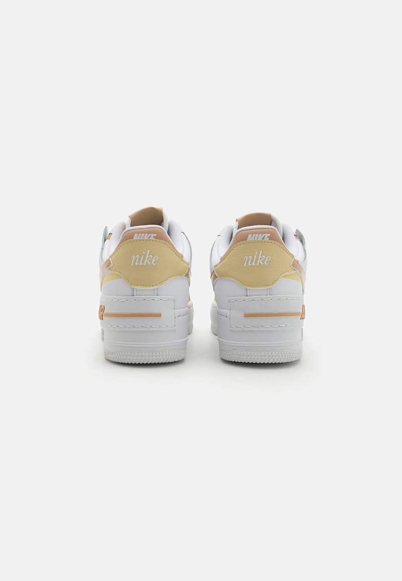 Zapatillas Nike blancas con acentos en tonos marrón y beige, suelas de goma texturizadas, cuellos acolchados y logo de la marca bordado en el talón.