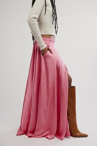 Falda larga de satén rosa con abertura lateral y bolsillos, combinada con una bota marrón hasta la rodilla. Suéter blanco cropped de canalé que se lleva por encima de la cintura.