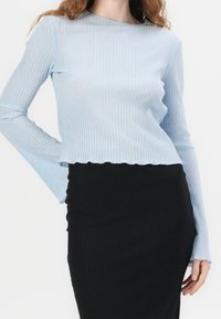 Haut bleu clair à manches longues avec une texture en ribbes, présentant un col rond et un ourlet court, associé à une jupe noire en ribbes.