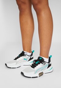 White and gray athletic shoes with black accents and turquoise trim. Features mesh material, laces, and a textured sole for grip.