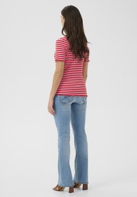 Rood-wit gestreepte top met korte mouwen en een scalloped zoom, gecombineerd met lichtblauwe flared jeans en bruine haksandalen. Achteraanzicht.