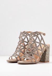 Sandali con tacco alto e cinturini in beige, con un tacco a blocco intrecciato, ritagli decorativi e abbelliti con strass per un tocco di brillantezza.