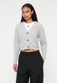 Cardigan gri scurt, cu decolteu în V, trei butoane și textură cu nervuri, asociat cu pantaloni negri cu talie elastică.