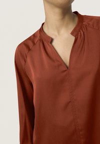 Blusa di raso rosso con scollatura a V e maniche lunghe, caratterizzata da una texture delicata e un dettaglio arricciato sul stern.