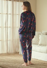 Pehmete kangaste kaksosaline koduriiete komplekt, millel on mereväesinine taust mitmevärviliste lillemustritega ja elastsete mansettidega pükstel.