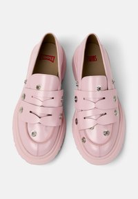 Zapatos rosas de tipo slip-on con correas decorativas, botones plateados y una suela acolchada, que exhiben un diseño moderno y juguetón.