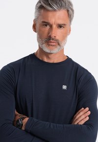 Laivan sininen pitkähihaisen t-paita, joka on valmistettu sileästä ja kevyestä kankaasta. Paidassa on pieni logo rinnassa ja pyöreä pääntie.