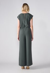 Tuta verde scuro con maniche corte, fascia elastica in vita e dettaglio a chiave sul retro. Realizzato in tessuto morbido con vestibilità rilassata.