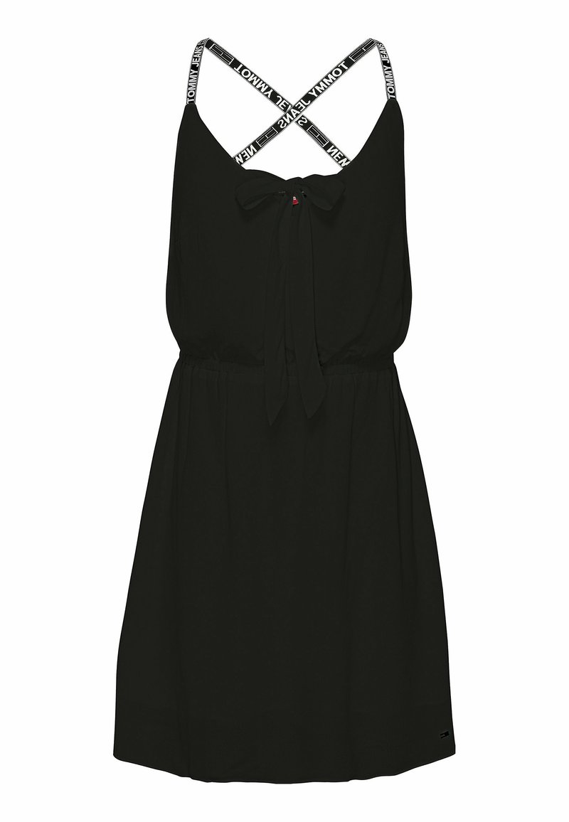 Black sleeveless dress with a tie front and crisscross white branded straps. Smooth texture and relaxed fit, featuring a cinched waist.