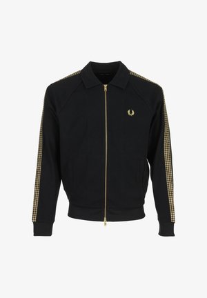 Veste noire zippée avec col, rayures dorées à motif damier sur les manches, et petit logo en laurier doré sur le côté gauche de la poitrine.