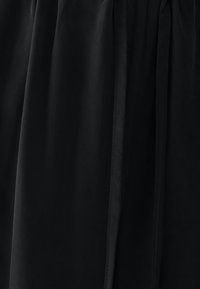 Sort stof med en glat, flydende tekstur; har folder og en bundet talje for justerbar pasform; minimalistisk design uden mønstre.
