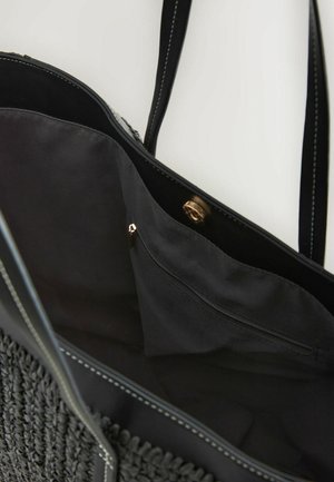 Melnā iepirkumu soma ar izstieptu tekstūru un gludām ādas akcentām, atvērta, lai atklātu plašu iekšpusi ar rāvējslēdzēja kabatu.