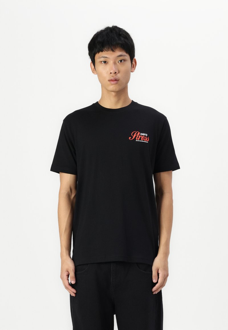 Black cotton t-shirt with short sleeves, round neckline. Features red text "zero Stress" on the chest. Simple design with a relaxed fit.