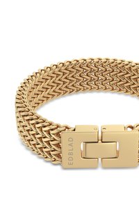 Kuldne metal käevõru, millel on punutud disain, sile pind ja ristkülikukujuline kinnis koos graveeritud brändinimega.