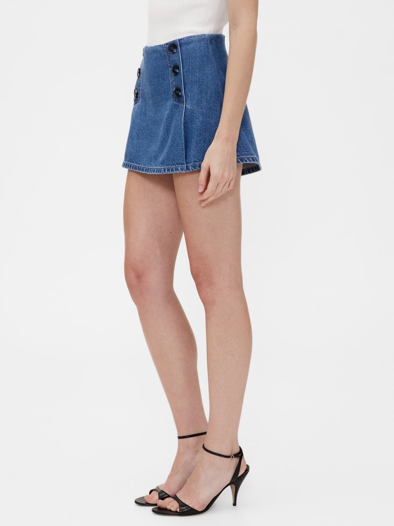 Denim minikjol med hög midja, utsvängd form, två sidofickor och fyra runda svarta knappar. Färgen är medelblå med fransad fåll.