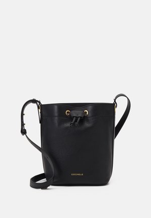 Bolso tipo cubo de cuero negro con correa de hombro ajustable, cierre con cordón y pequeño logo dorado en el centro inferior.