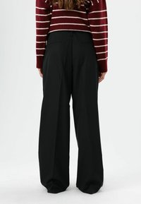 Zwarte broek met wijde pijpen gemaakt van gladde stof, met een getailleerde snit, twee achterzakken en een nette tailleband.