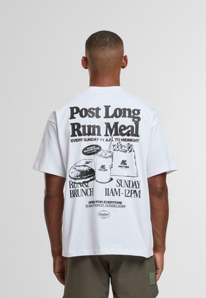 Man wearing white T-shirt with black print promoting a Sunday brunch from 11 AM to midnight, featuring burger, drink, and fries illustration.