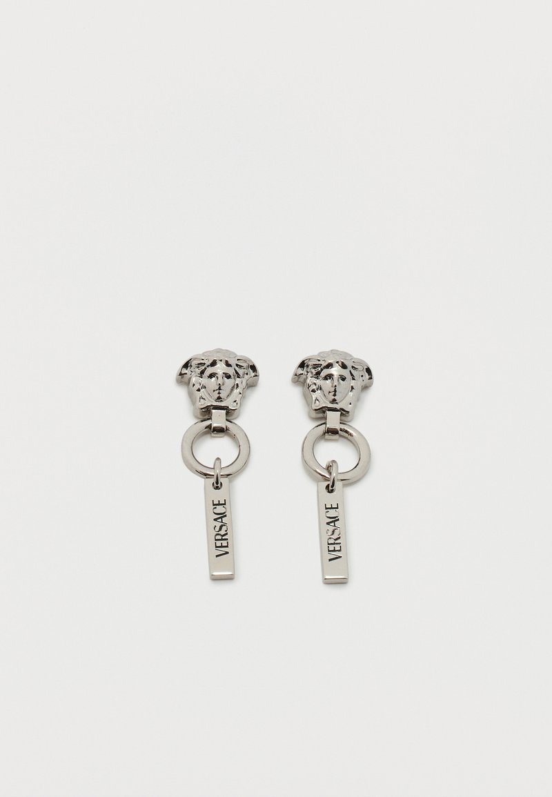 Uhani z netom srebrne barve z glavo Meduze, krožnim členkom in vertikalnimi obeski z gravuro "VERSACE", ki visijo spodaj.
