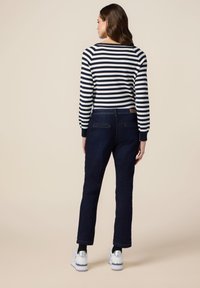 Suéter a rayas en navy y blanco con mangas largas, combinado con jeans azul oscuro. El modelo lleva zapatillas blancas con detalles plateados.