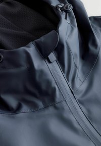 Giacca impermeabile in blu scuro, con colletto alto, texture liscia e zip frontale con coulisse regolabile per una vestibilità sicura.