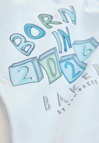 Witte katoenen outfit met de tekst "BORN IN 2026" in kleurrijke blokletters en cijfers. Inclusief metalen drukknoopjes voor eenvoudig aan- en uittrekken.