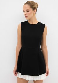 Robe sans manches noire avec un corsage ajusté et une jupe évasée, dotée d'un ourlet plissé blanc. Le tissu semble lisse et structuré.