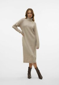 Bežna pletena obleka s turtleneck ovratnikom in dolgimi rokavi, rebrastimi manšetami in robom; oblečena z rjavimi gleženjskimi škornji, ki poudarjajo oprijet silhueto.