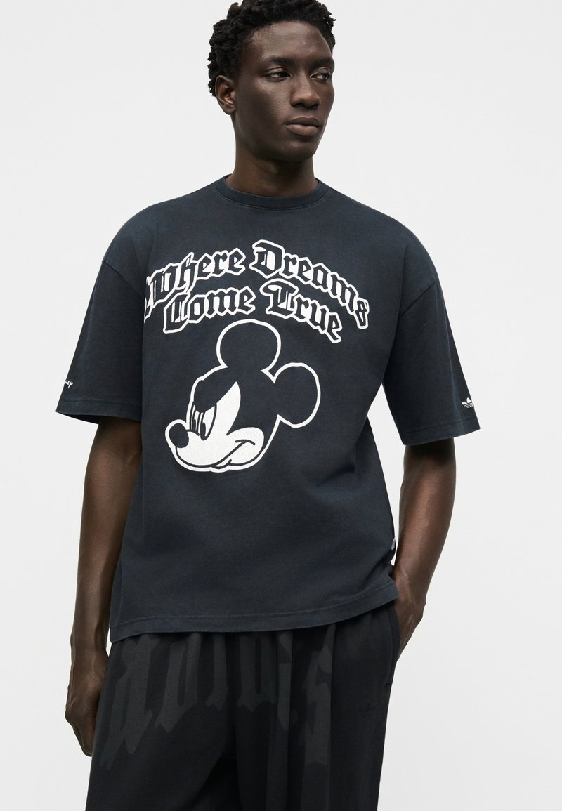 Mand iført en sort oversized t-shirt med en stor hvid Mickey Mouse-grafik og teksten "Hvor drømme går i opfyldelse."