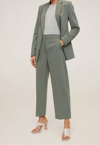 Costume ajusté vert clair avec une veste cintrée, un pantalon droit et un haut gris clair. Présente un tissu doux et un design minimaliste.