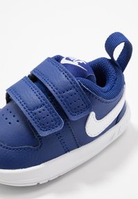 Niebieski sneaker z syntetycznej skóry, dwa paski na rzepy, siateczkowe wnętrze, białe akcenty, perforowany nos i pętla na pięcie.