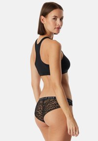 Zwarte sportbeha met een racerback ontwerp, gecombineerd met zwarte kanten hipsterpanty’s met een geprinte textuur en een merkband.